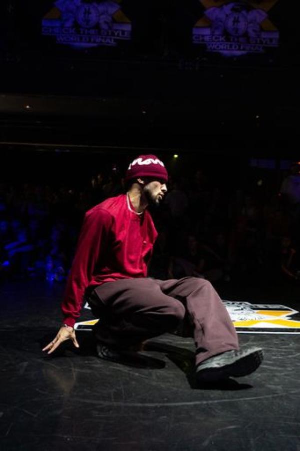 Kieron in mid performance, on a stage but angled to only focus on him, in the middle of breaking or breakdancing, 