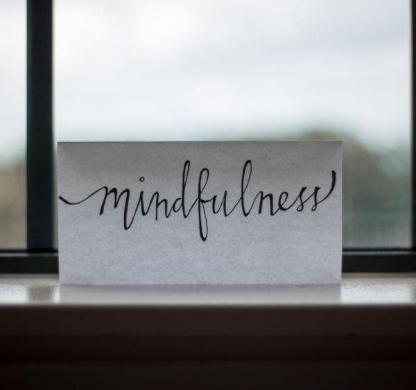 Mindfulness is written in script on a piece of paper and propped up on a windowsill.