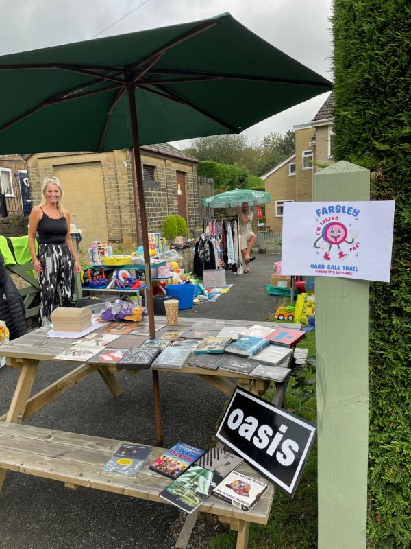 image displays a stall in a previous yard sale selling items at the front of their house with the home owner present