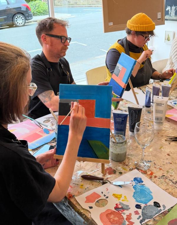 image shows people painting David Hockney's "A Bigger Splash" using acrylic paints. 