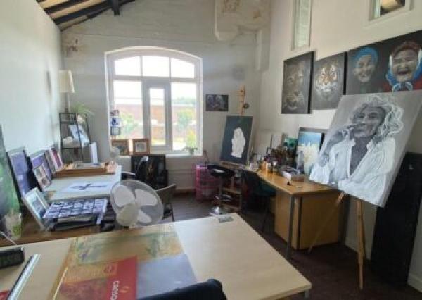 photo of inside the studios, an artists pod is in view, filled with proffessional paintings, with desks materials in an orderly layout
