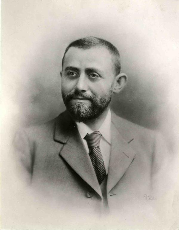 Black and white photograph of Michael Marks. He wears a suit, shirt and tie, and has a short beard.