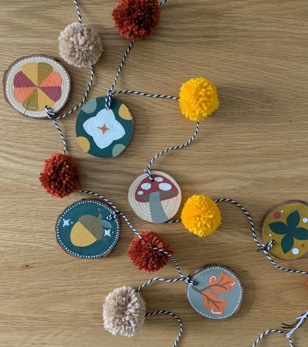 A string of pompoms and handpainted wooden pendants with Autumnal designs
