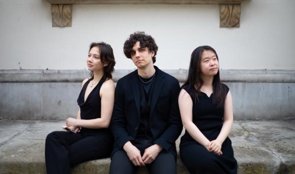 Three musicians dressed all in black sat back to back. 