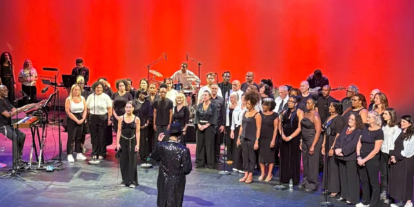 A choir and orchestra perform on stage, illuminated by dramatic red lights.
