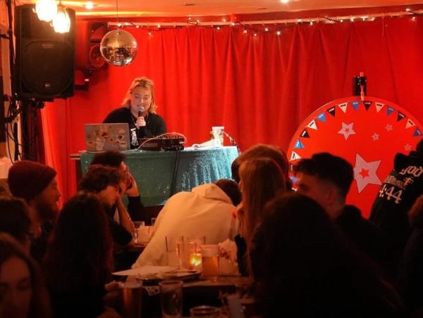 A quizmaster reads questions to a busy room.