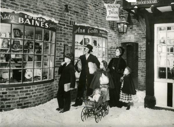 A black and white photograph of a family browsing a recreated Victorian street scene covered in snow (Abbey House Museum).