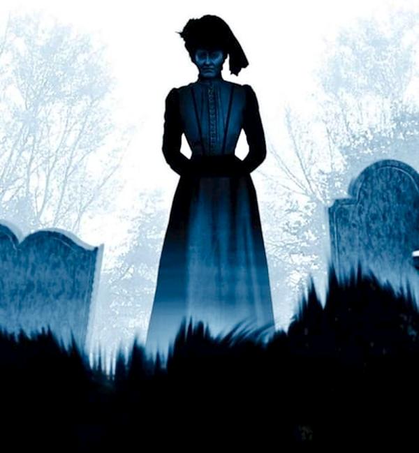 A dark figure of a woman dressed in Victorian attire. Standing amongst grave stones. 