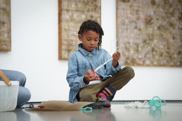 A child sat on the floor of an art gallery, playing with a white twig