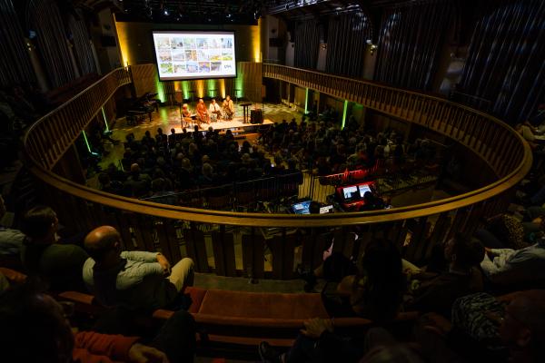 A large audience watches a panel discussion in the Howard Assembly Room.