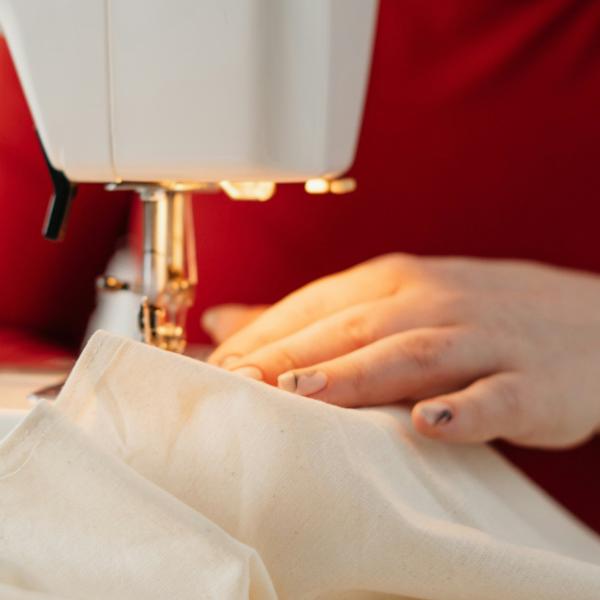 A close up photo of someone holding white fabric as it's running through a sewing machine.