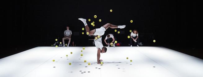 Dancer balanced on one hand in a swirl of tennis balls