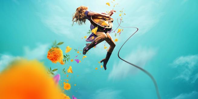 A woman mid jump holding a guitar against a blue sky with clouds