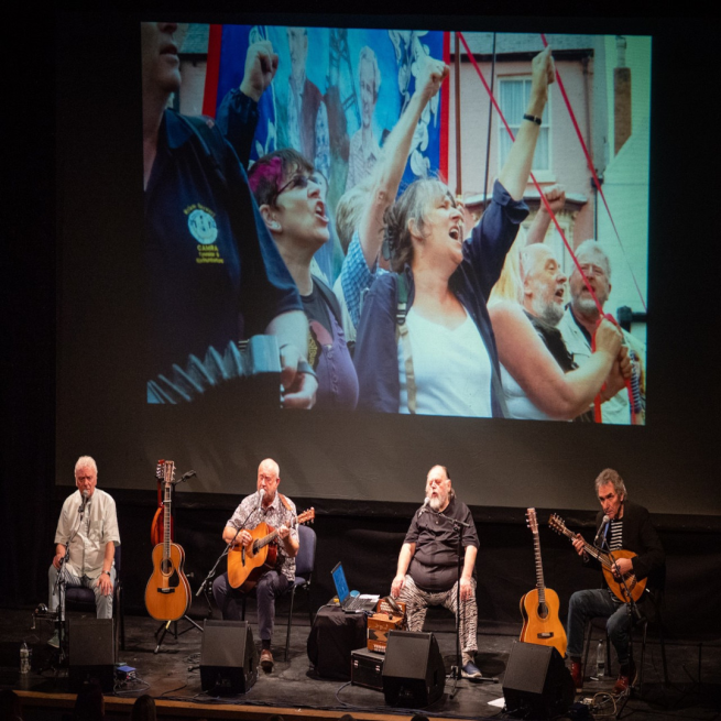 The Pitmen Poets on stage playing instruments.