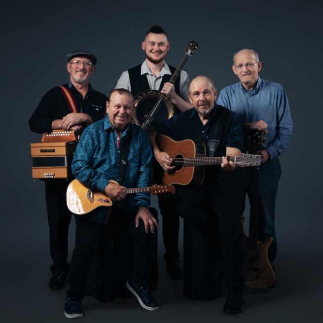 Members of The Fureys stand together. They hold various instruments from guitars to banjos.