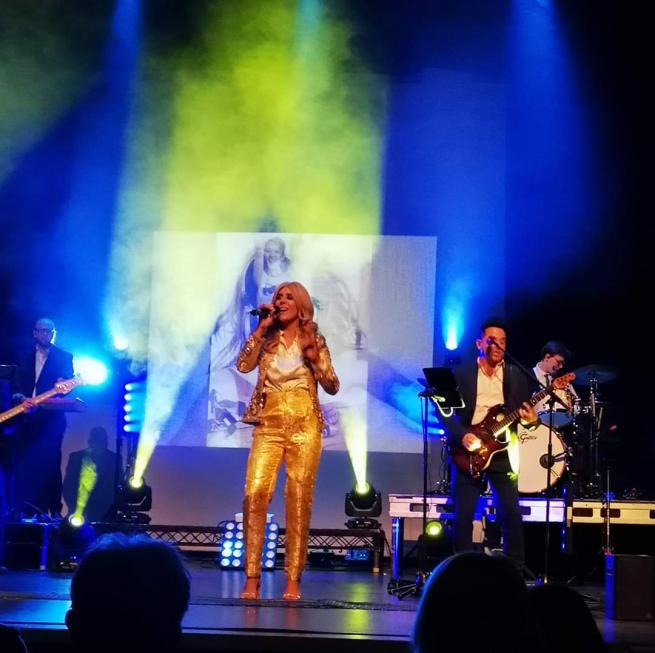 Alexandra Darby performing on stage. She is wearing a yellow suit. 