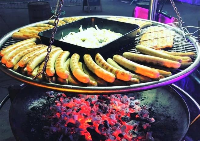 a round pan of coals with a bratwurst packed grill pan suspended above