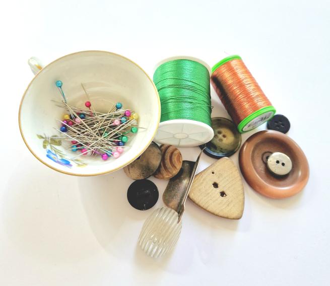 A tea cup full of pins, two bobbin reels and a handful of odd buttons