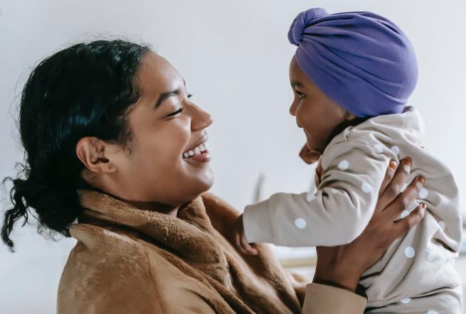 A mother lifting her baby in the air, they are both smiling.