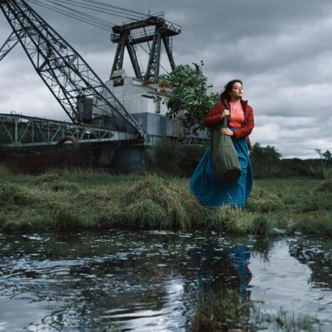 a young woman stands looking in the distance by water