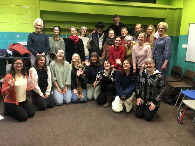 A group of people, gathered together for a photograph after a session. Smiling, waving hands and some singing. Ages 17 - 60+. 