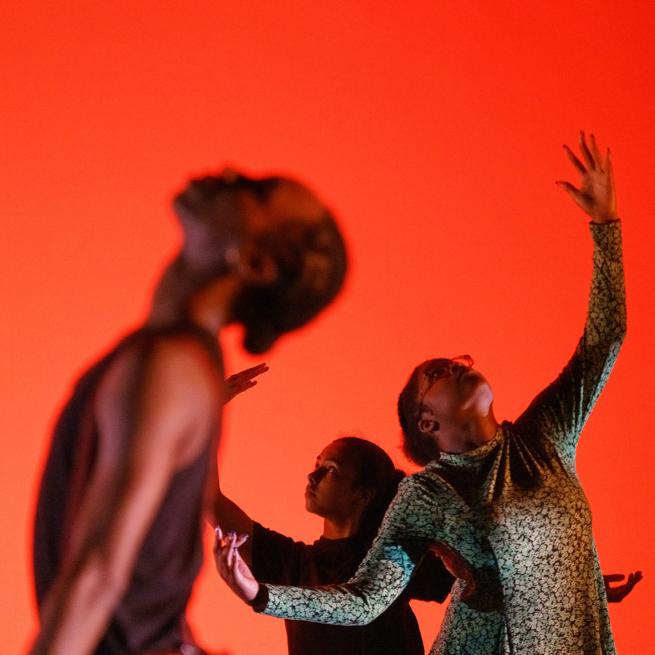 Three young dancers looking up, in front of a bright red/orange backdrop