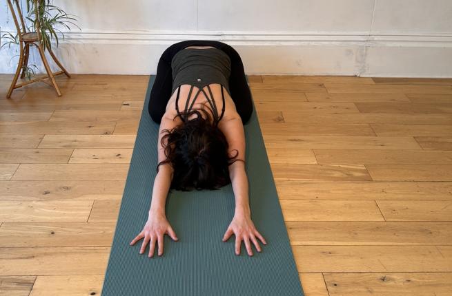 yoga teacher lady in childs pose in a green top on a green mat