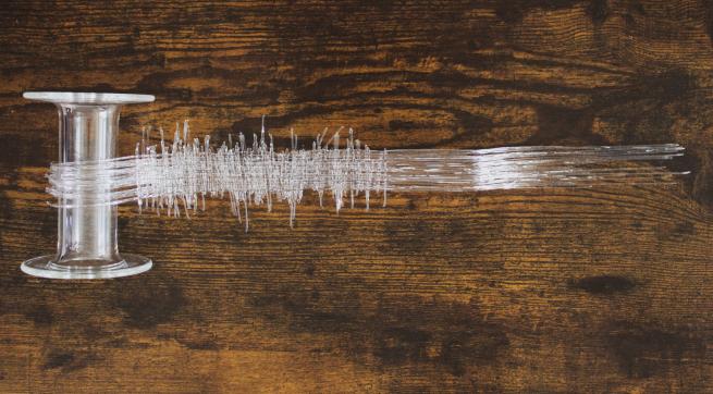 Glass bobbin with a piece of woven glass fabric laid on a wooden surface