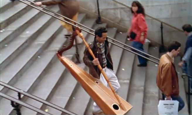 A man walks down into the metro carrying a huge wooden harp.