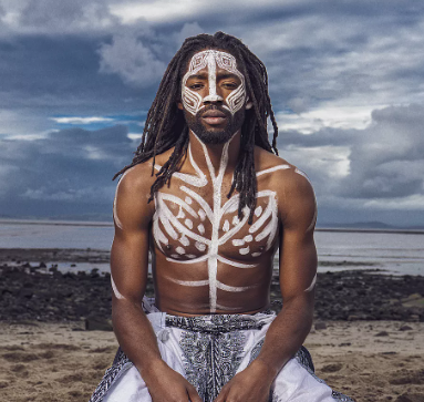 Man on beach looking at camera with white pattern painted on his chest and face.