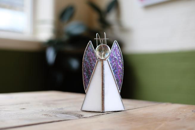 A white glass angel tops a wooden table. The angel has iridescent glass wings and a silver halo.