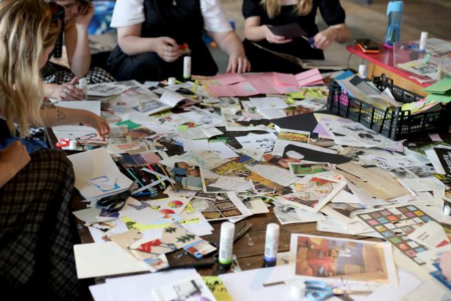 Image shows 5 people sat round a low table filled with colourful and patterned paper scarps, each person is cutting and sticking the paper.