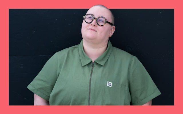 A bald woman wearing thick glasses and a green jumpsuit.
