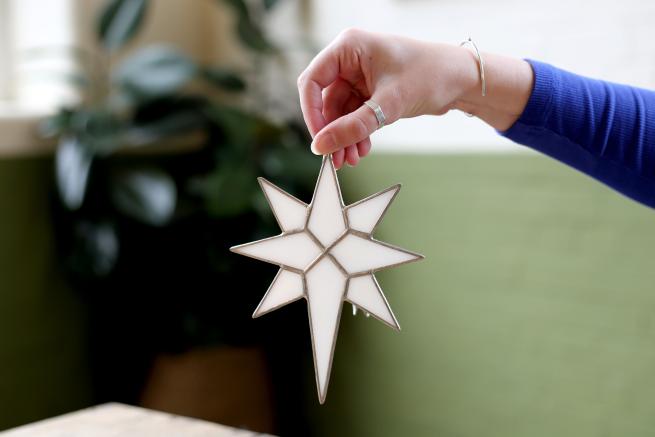 A white stained glass eight point star is held in place by a woman's hand wearing a blue long sleeve tshirt.