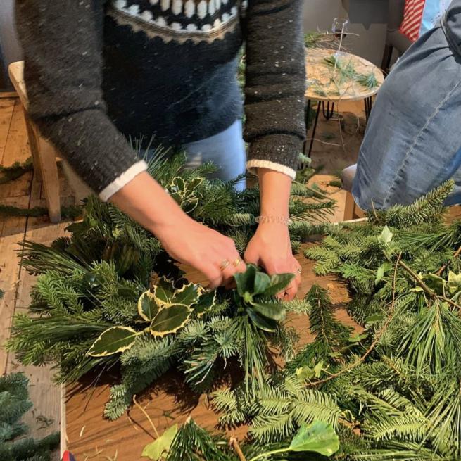 A photograph of hands placing winter foliage into a wreath