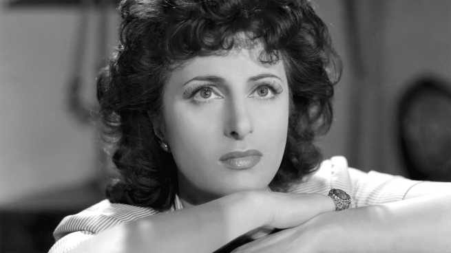 A woman rests her head on her hands, she is staring into the distance.