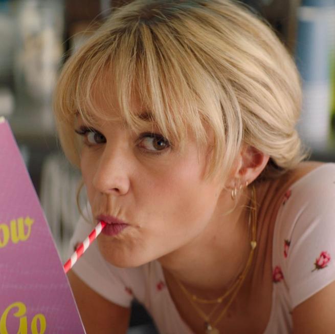 a woman drinks through a striped paper straw whilst holding a book, she is looking at the camera
