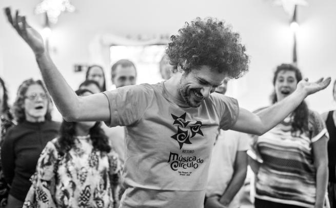 Singing leader standing in the middle of a circle of singers with smile on face and hands in the air