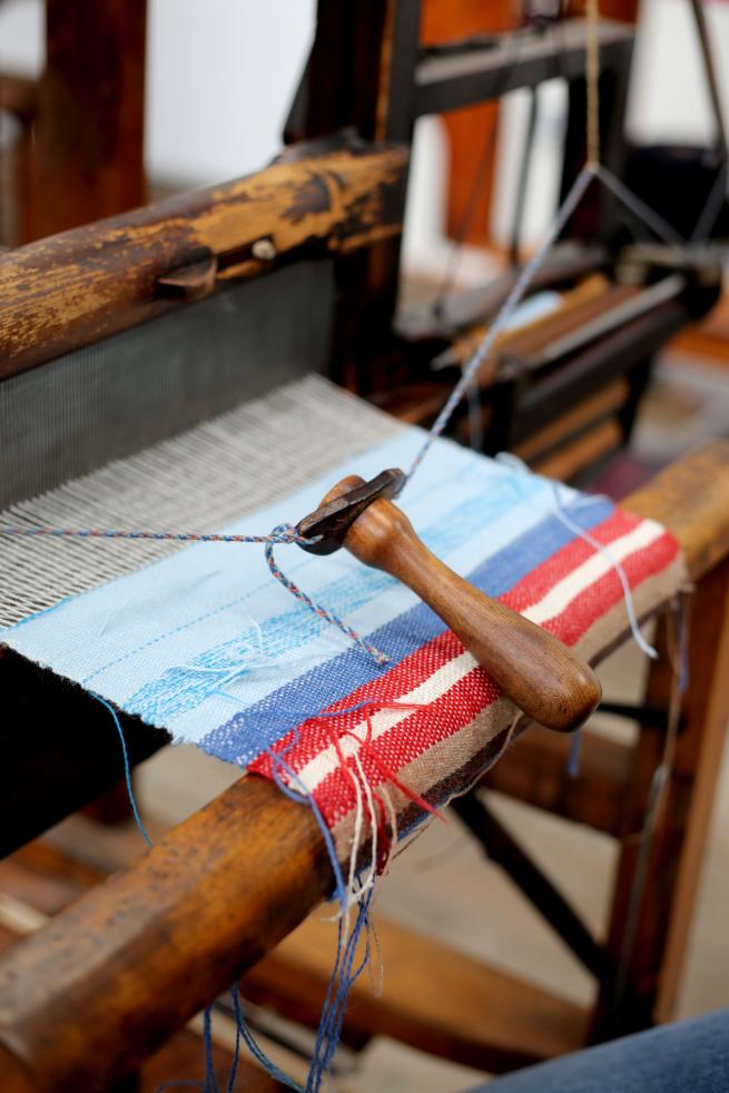A close up of the dark wooden loom with a blue and red striped woven sample.