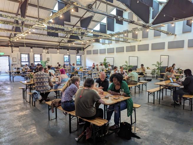 A large, spacious and light room with people sitting at tables playing board games. 