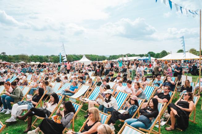 We're focused on a snapshot of last years busy North Leeds Food Festival whereby festival goers are lounged on deckchairs enjoying the live music!