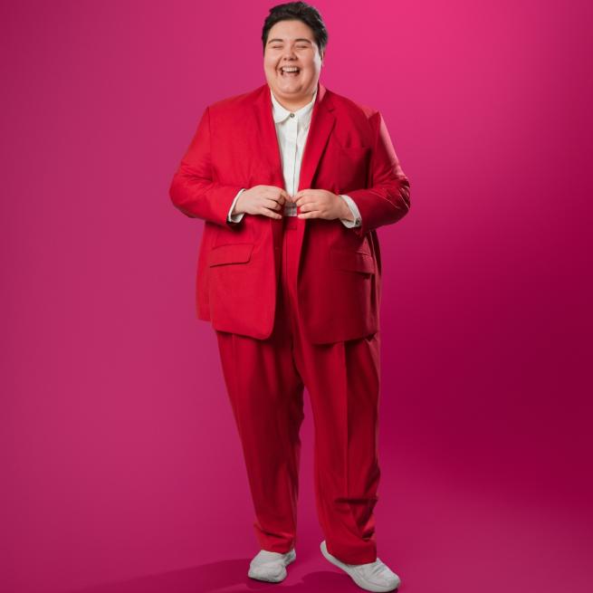 Sofie Hagen stood in a red suit with a dark pink background.