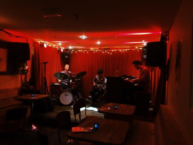 3 musicians play on a red lit stage.