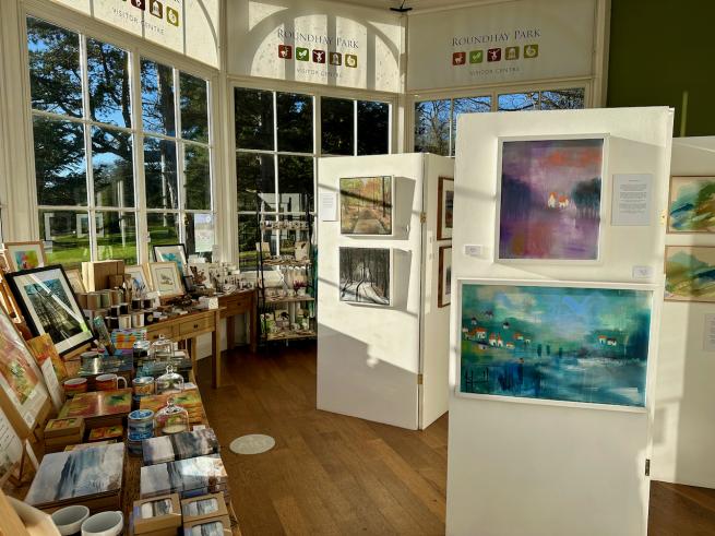The image shows the gallery space with art displayed on panels and gifts