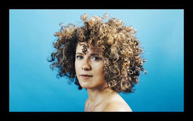 A woman with lots of curly hair stood against a blue background.