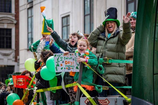 little girl on a float waving a hand painted poster which says Happy St Patricks Day.