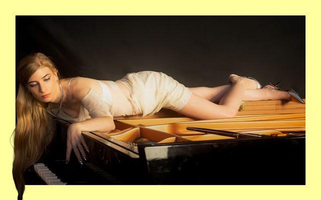 A woman with blonde hair lying on top of a piano.