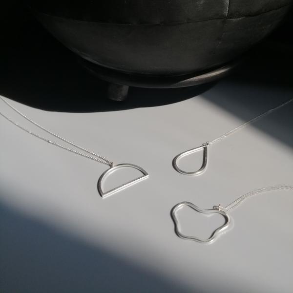 Three silver minimalist necklaces on a grey background