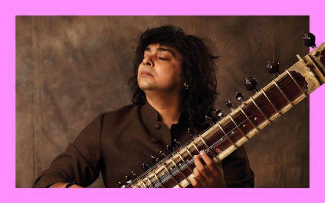 A man with a big head of hair holding a sitar.