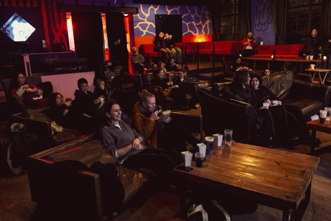 Image of cinema style set up, sofas and tables in darkly lit room